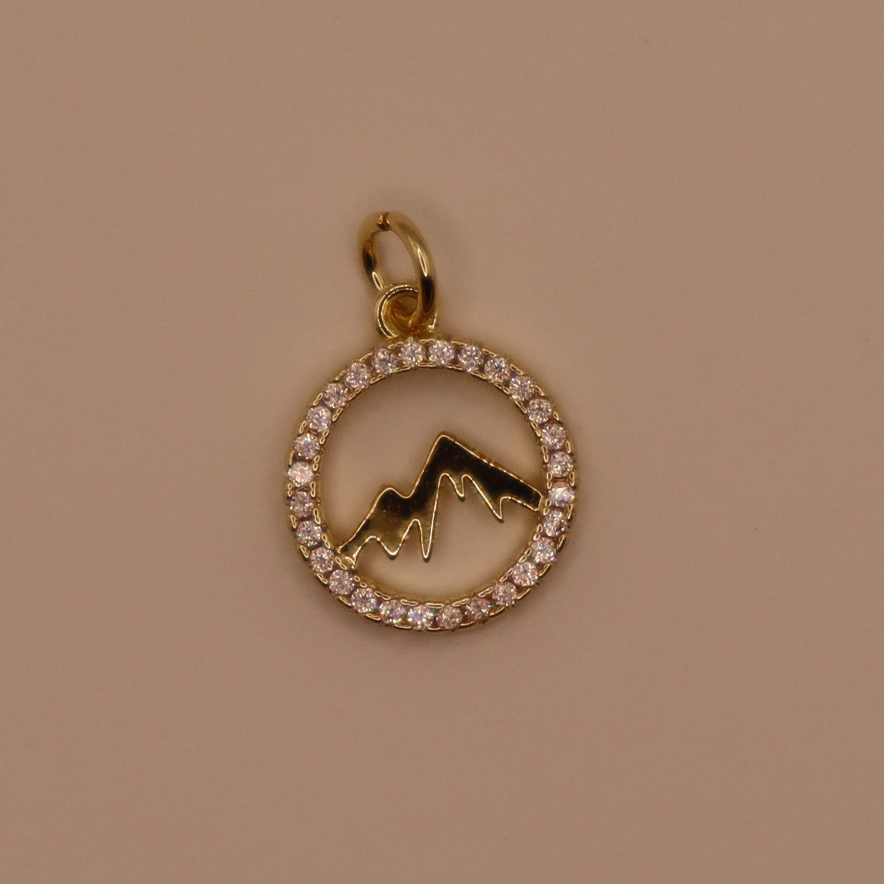 Gold charm with mountain design and diamond accents on a brown background