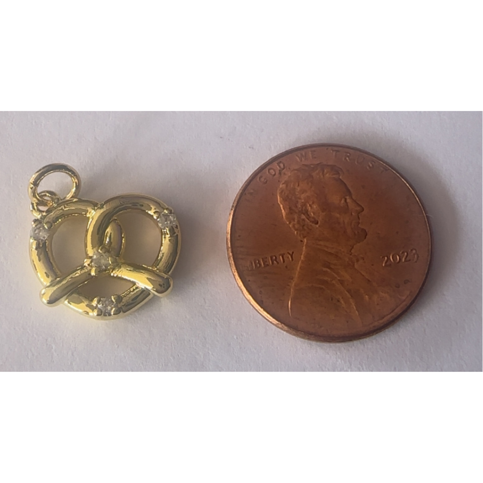 Gold pretzel-shaped charm next to a penny on a white background