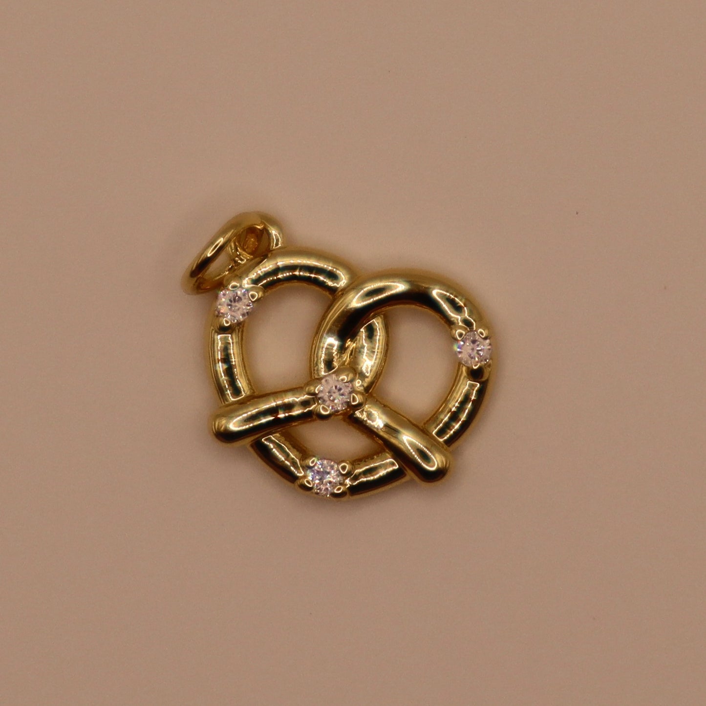 Gold pretzel-shaped pendant with embedded stones on a beige background