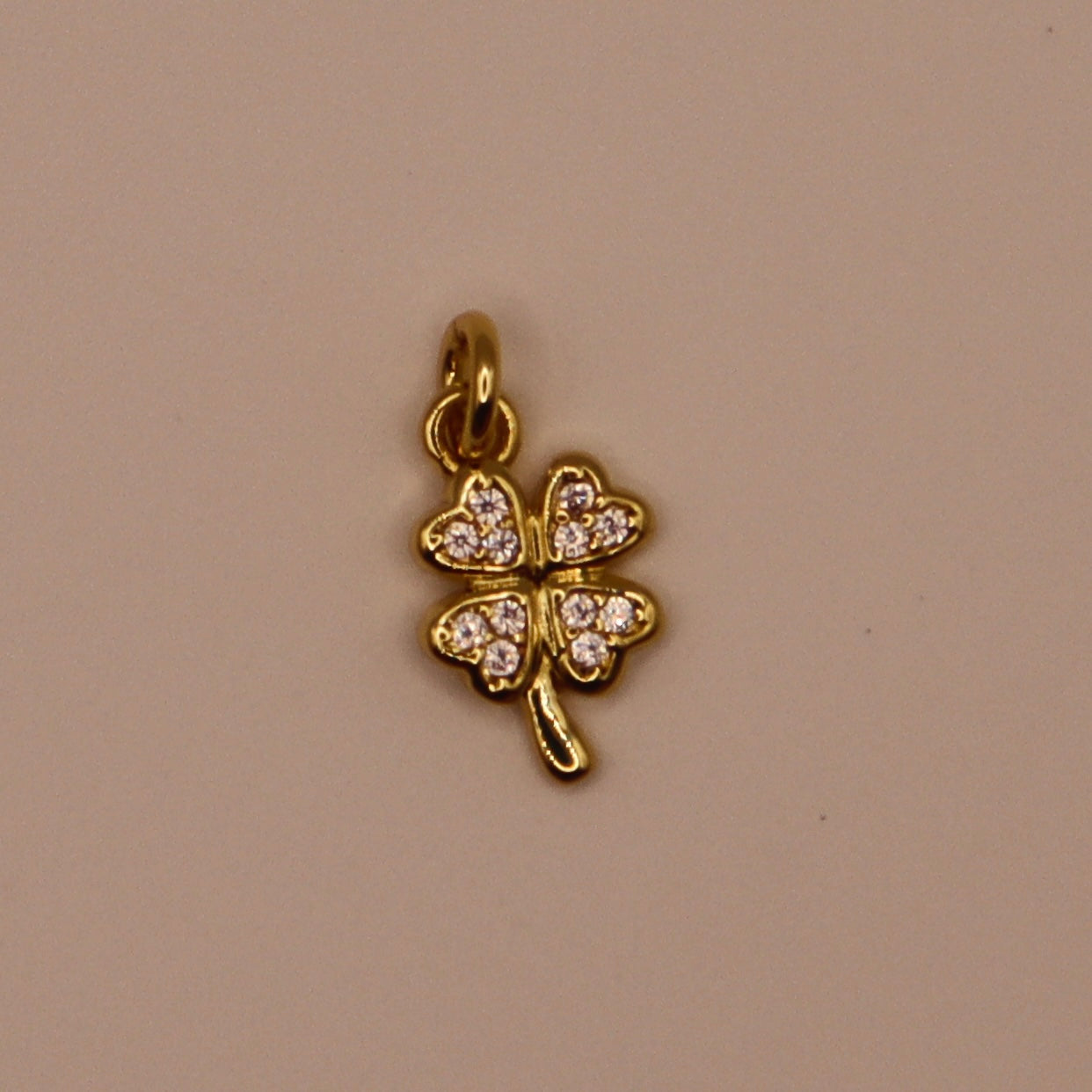 Gold four-leaf clover charm with embedded stones on a beige background