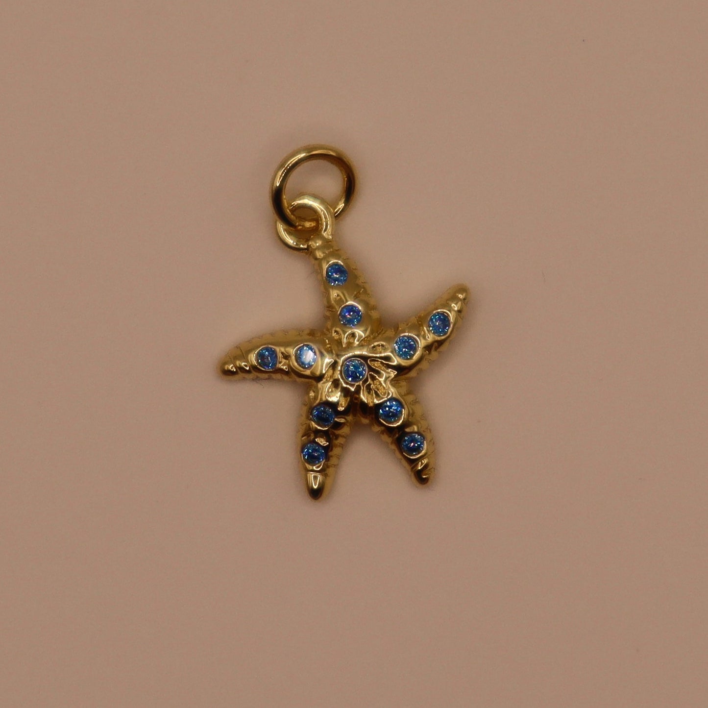 Gold starfish charm with blue stones on a beige background