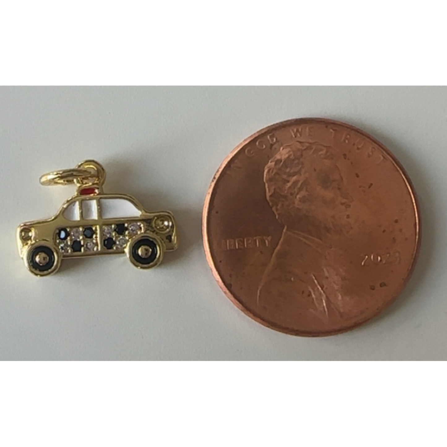 Gold car charm next to a penny on a white background