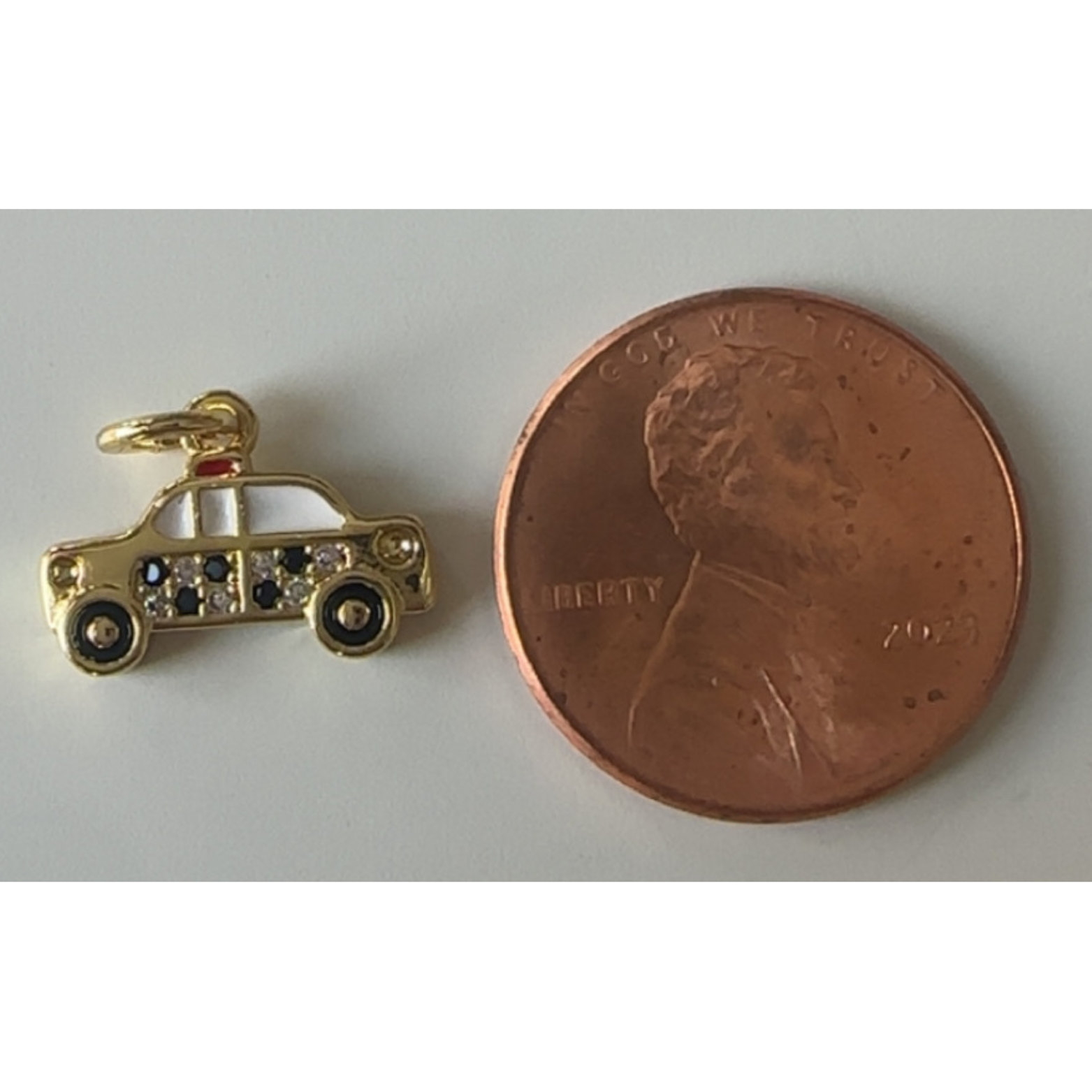 Gold car charm next to a penny on a white background