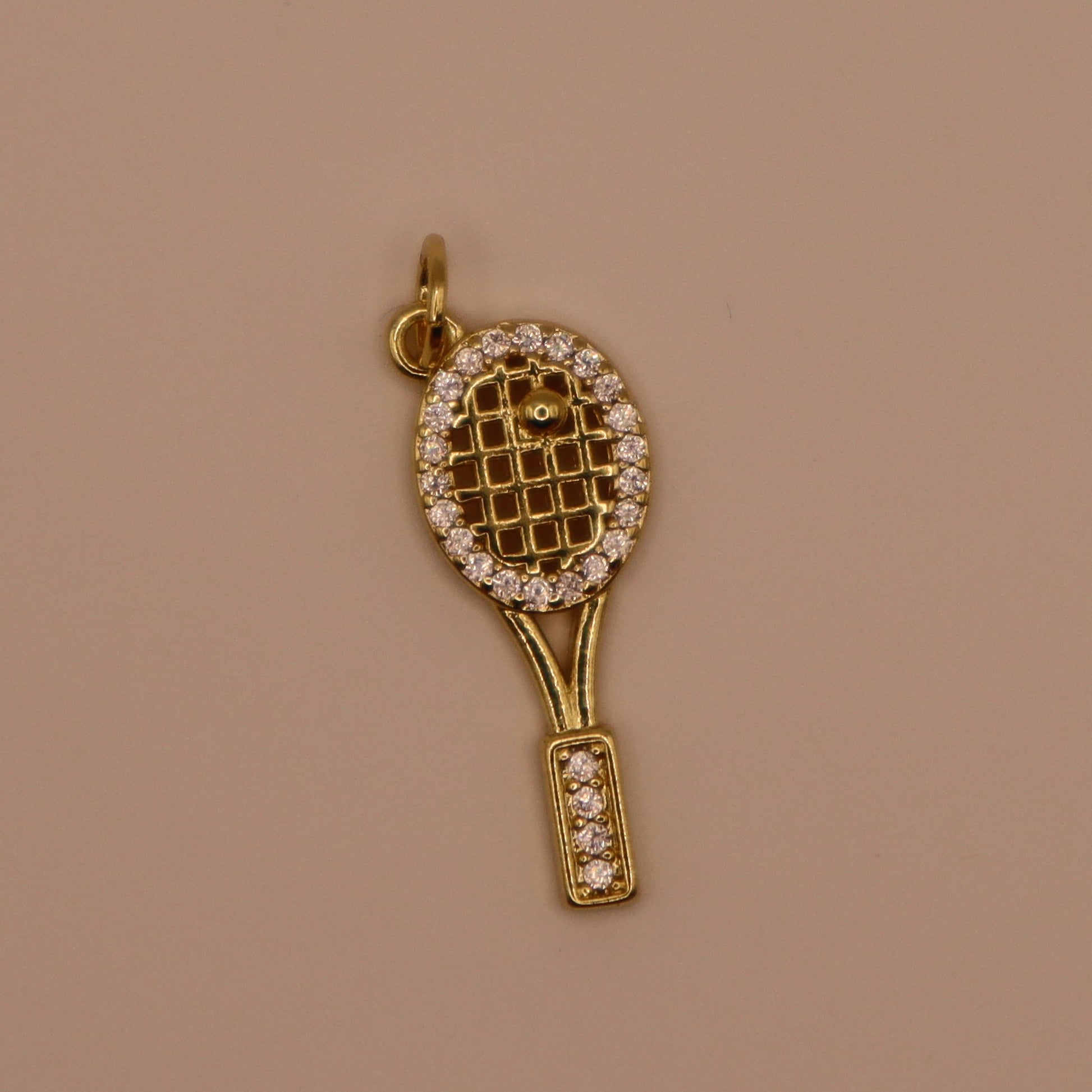 Gold tennis racket charm with diamonds on a beige background