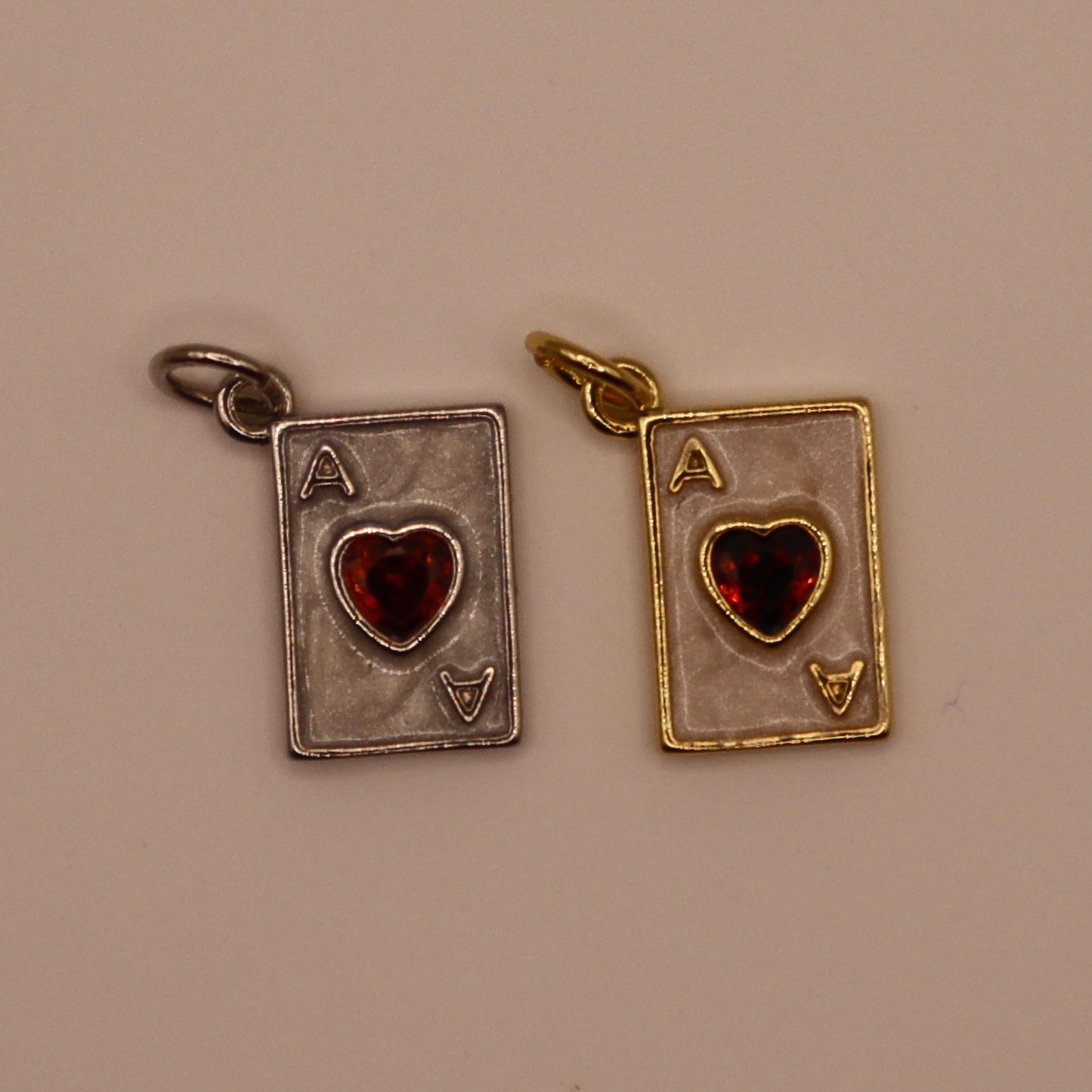Two playing card charms, one silver and one gold, on a beige background.