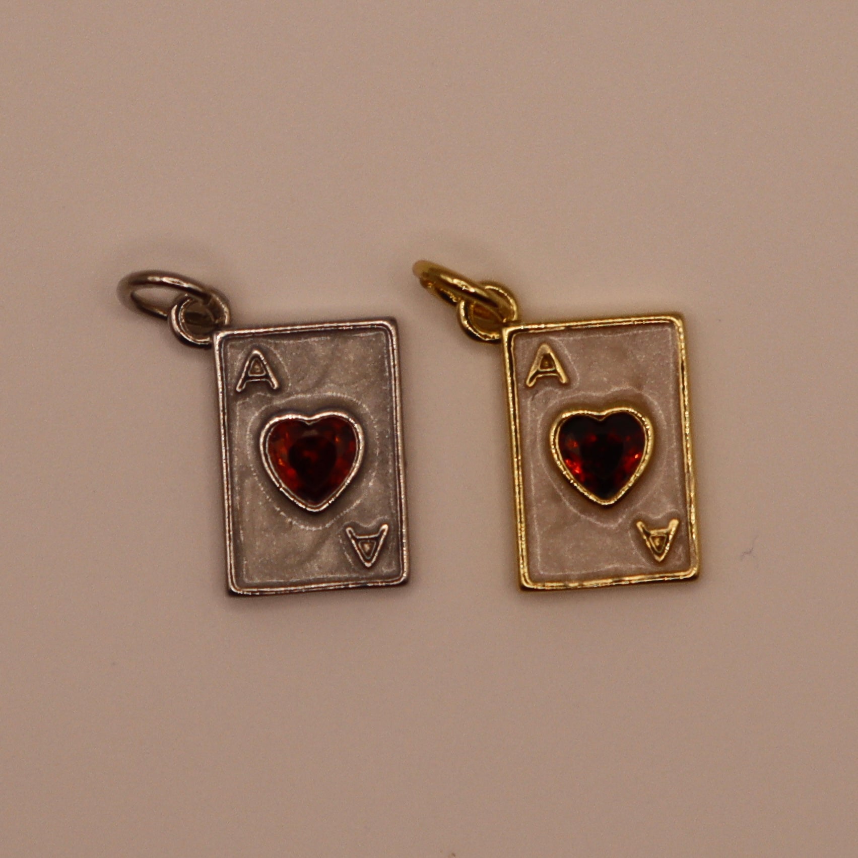 Two playing card charms, one silver and one gold, on a beige background.