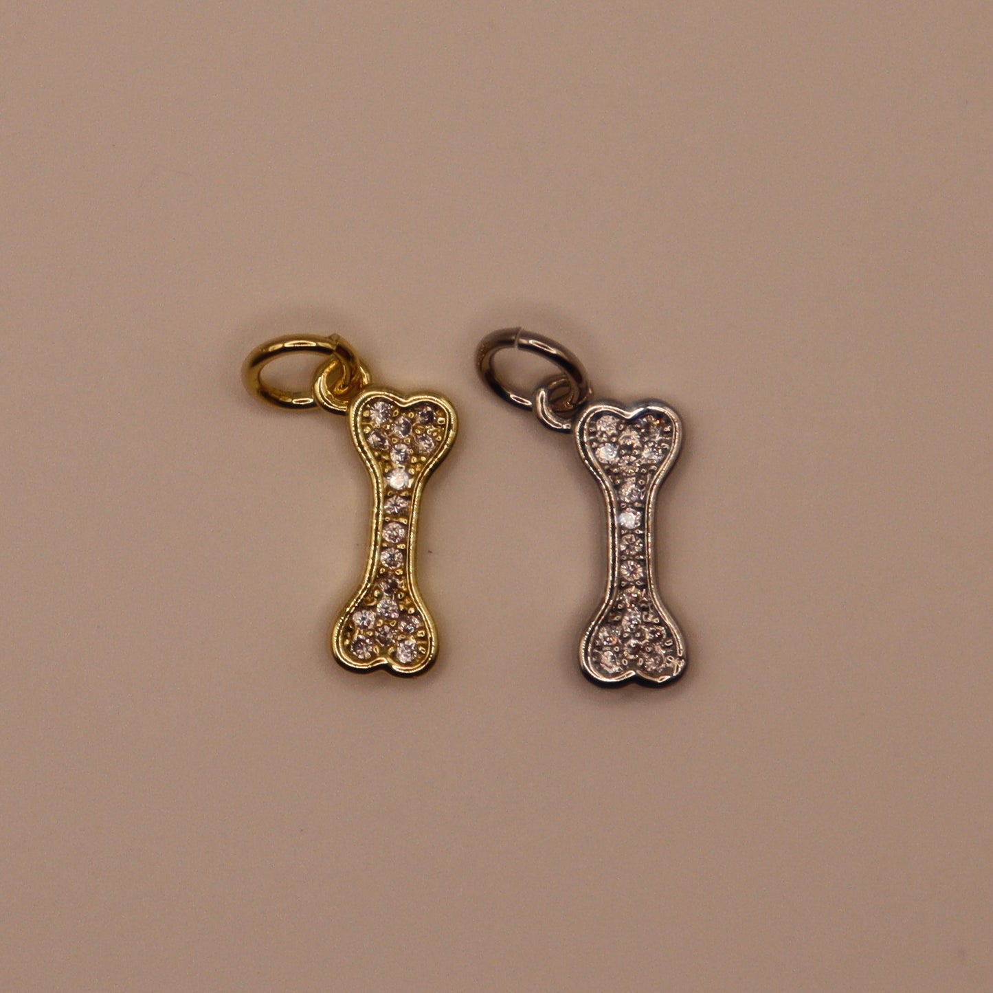 Gold and silver bone-shaped charms with rhinestones on a beige background