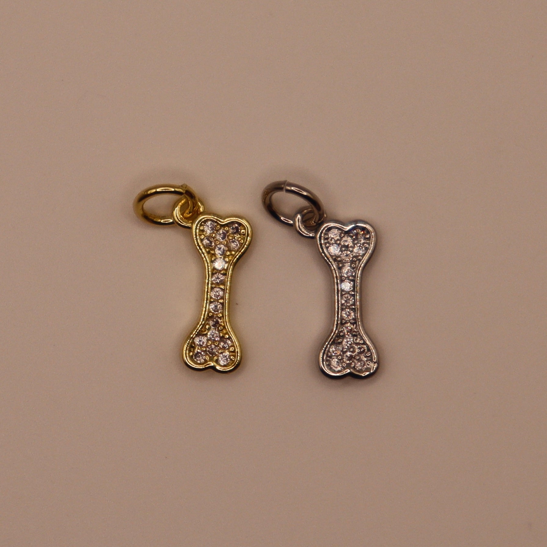 Gold and silver bone-shaped charms with rhinestones on a beige background