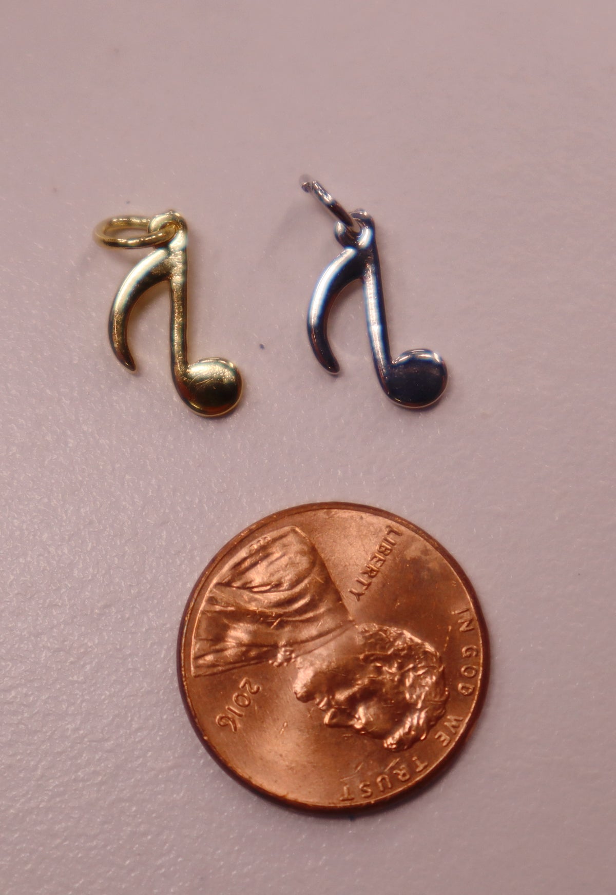 Note Charms Two musical note charms, one gold and one silver, next to a penny on a ...
