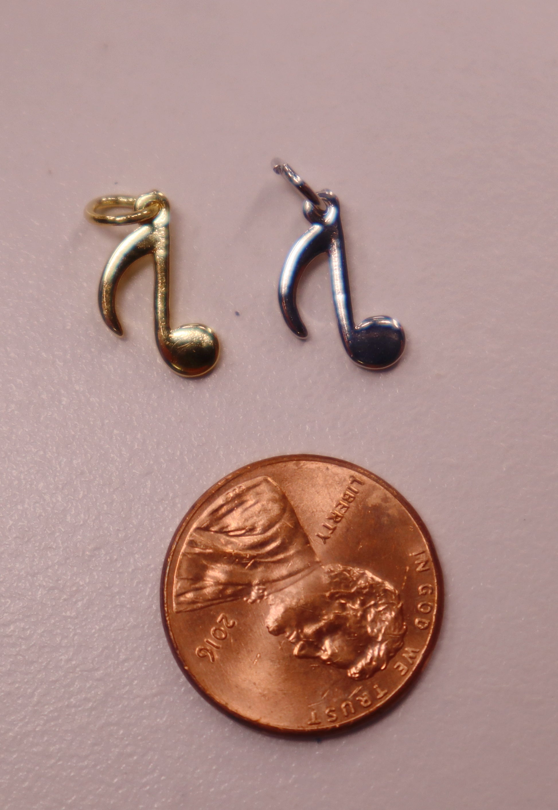 Two musical note charms, one gold and one silver, next to a penny on a pink background.