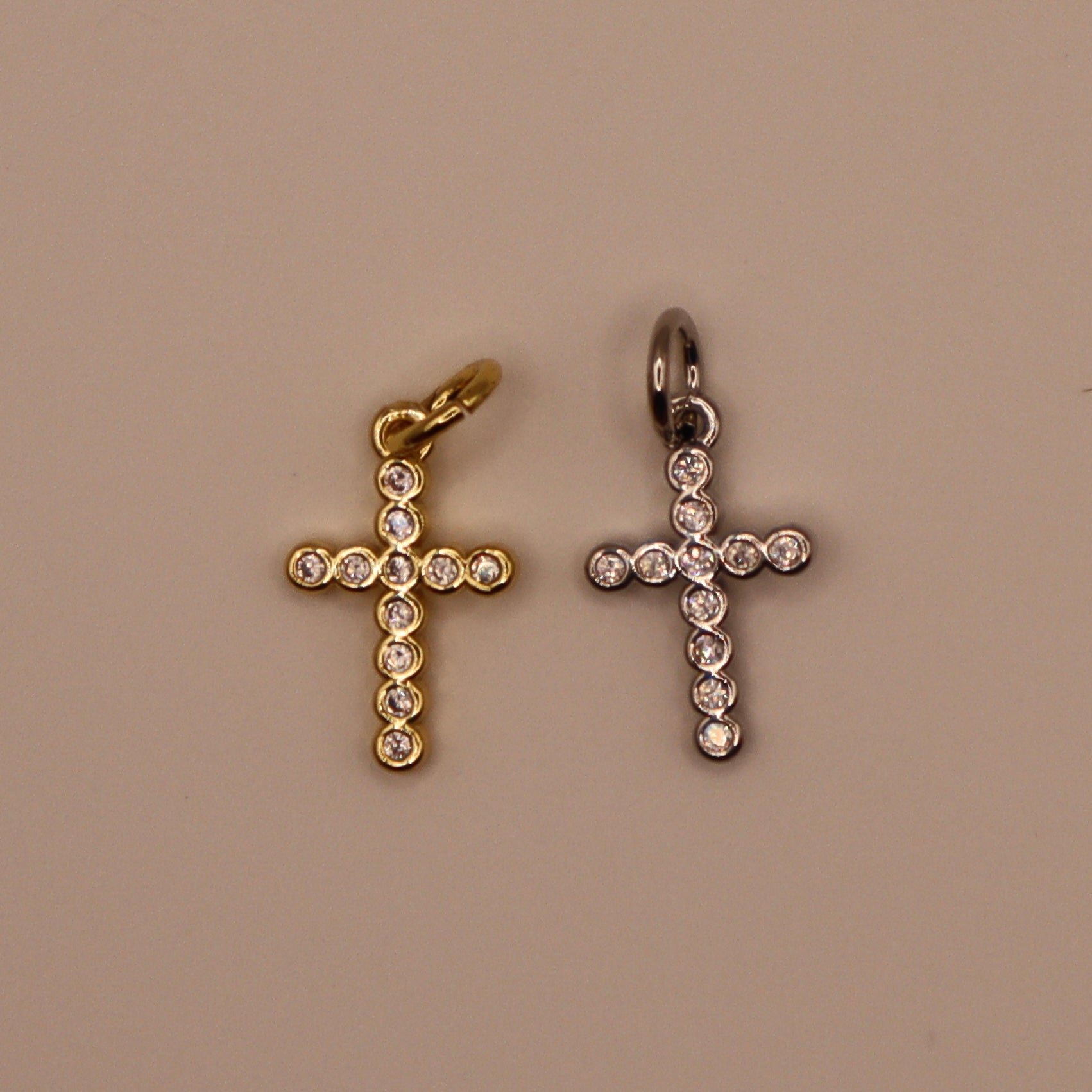 Two cross-shaped pendants, one gold and one silver, on a beige background.