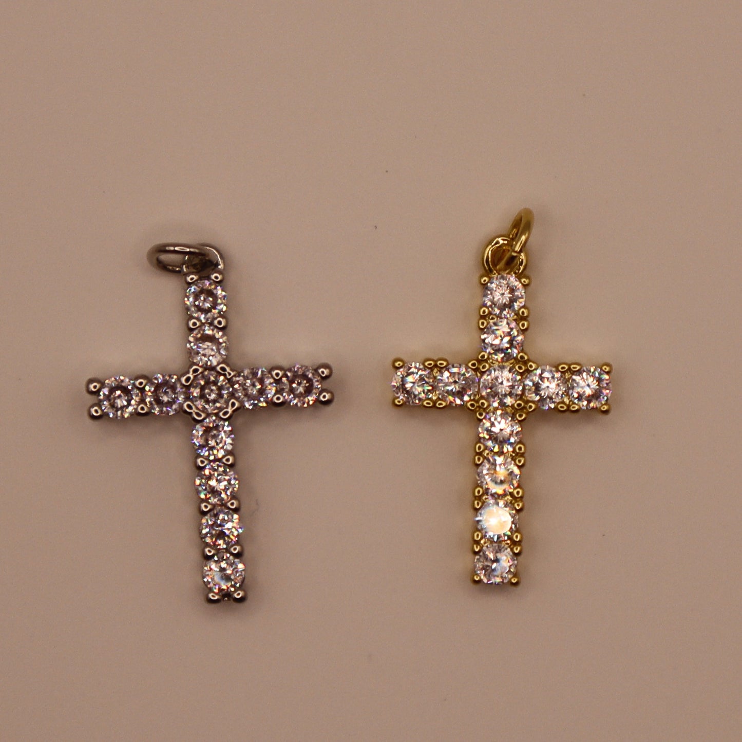 Two cross-shaped pendants, one gold and one silver, on a beige background.