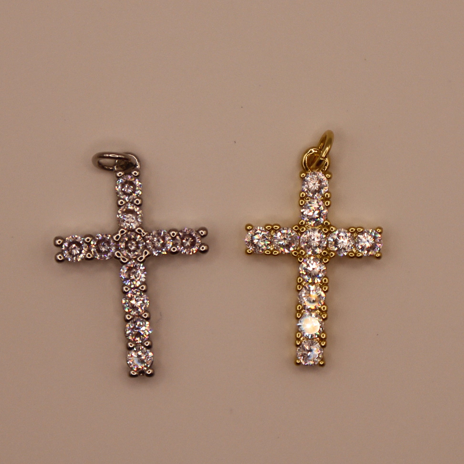 Two cross-shaped pendants, one gold and one silver, on a beige background.