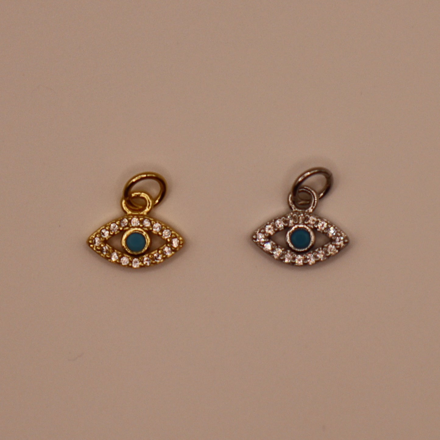 Two evil eye charms with blue centers and gold and silver borders on a beige background.