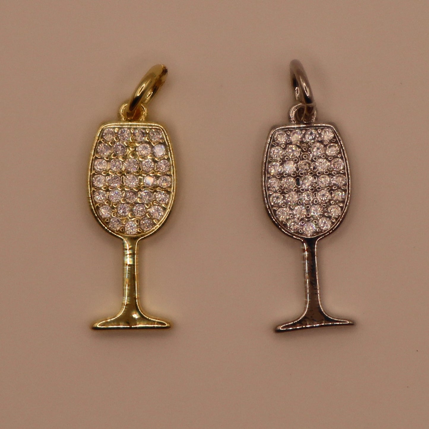 Two wine glass-shaped pendants, one gold and one silver, on a beige background.