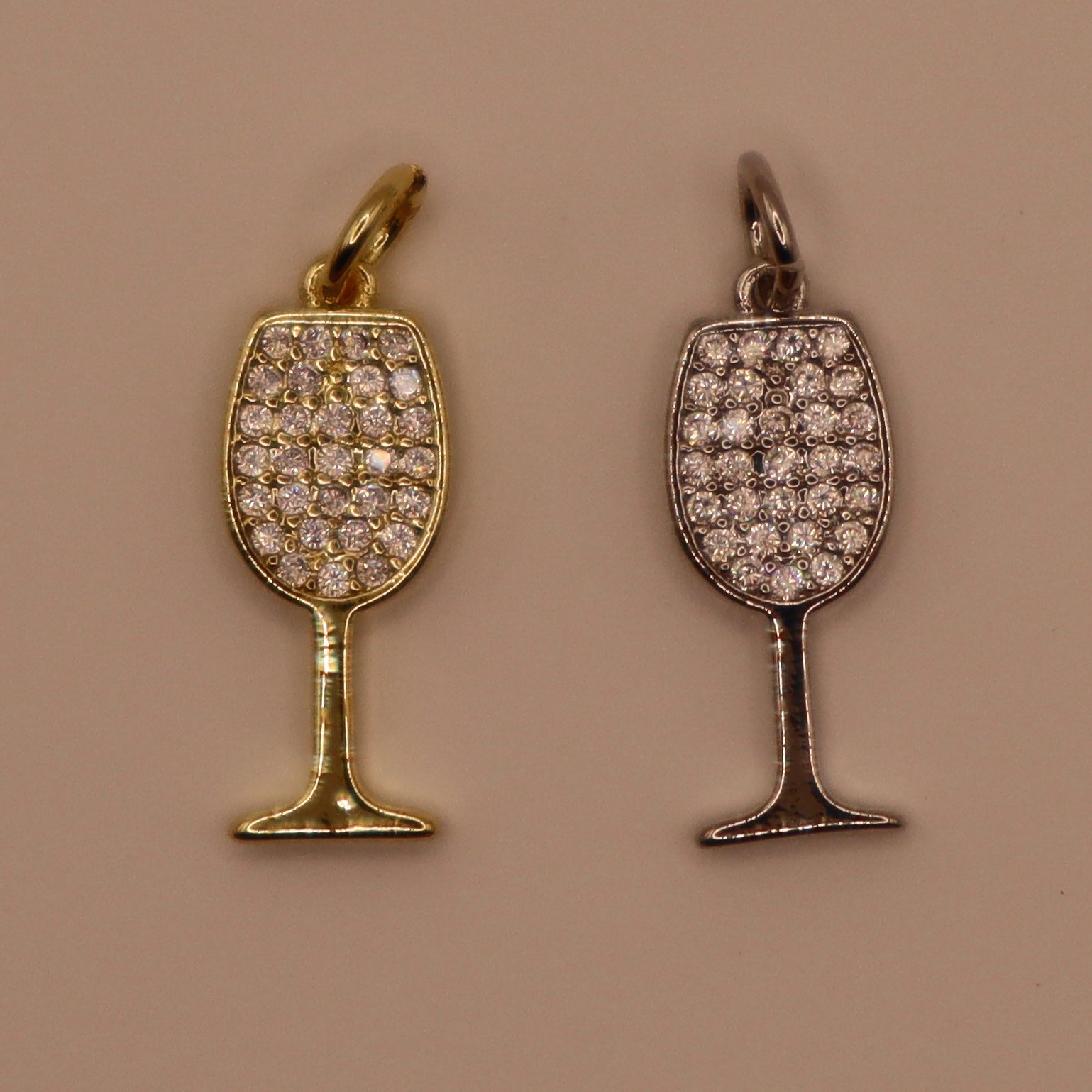 Two wine glass-shaped pendants, one gold and one silver, on a beige background.