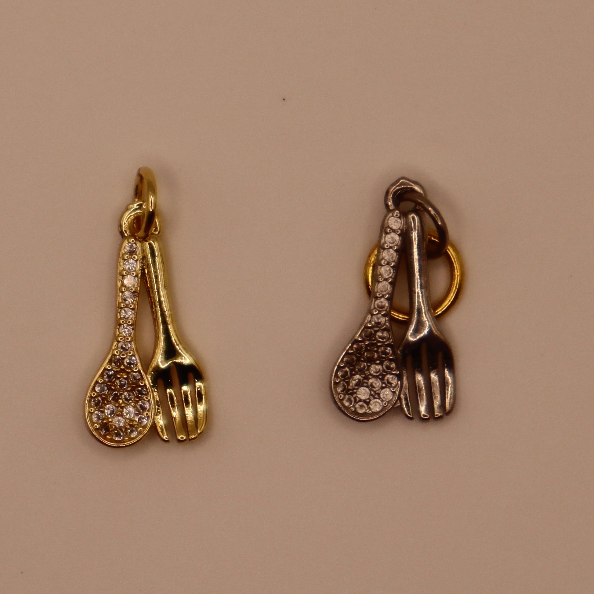 Gold and silver spoon and fork charms on a beige background
