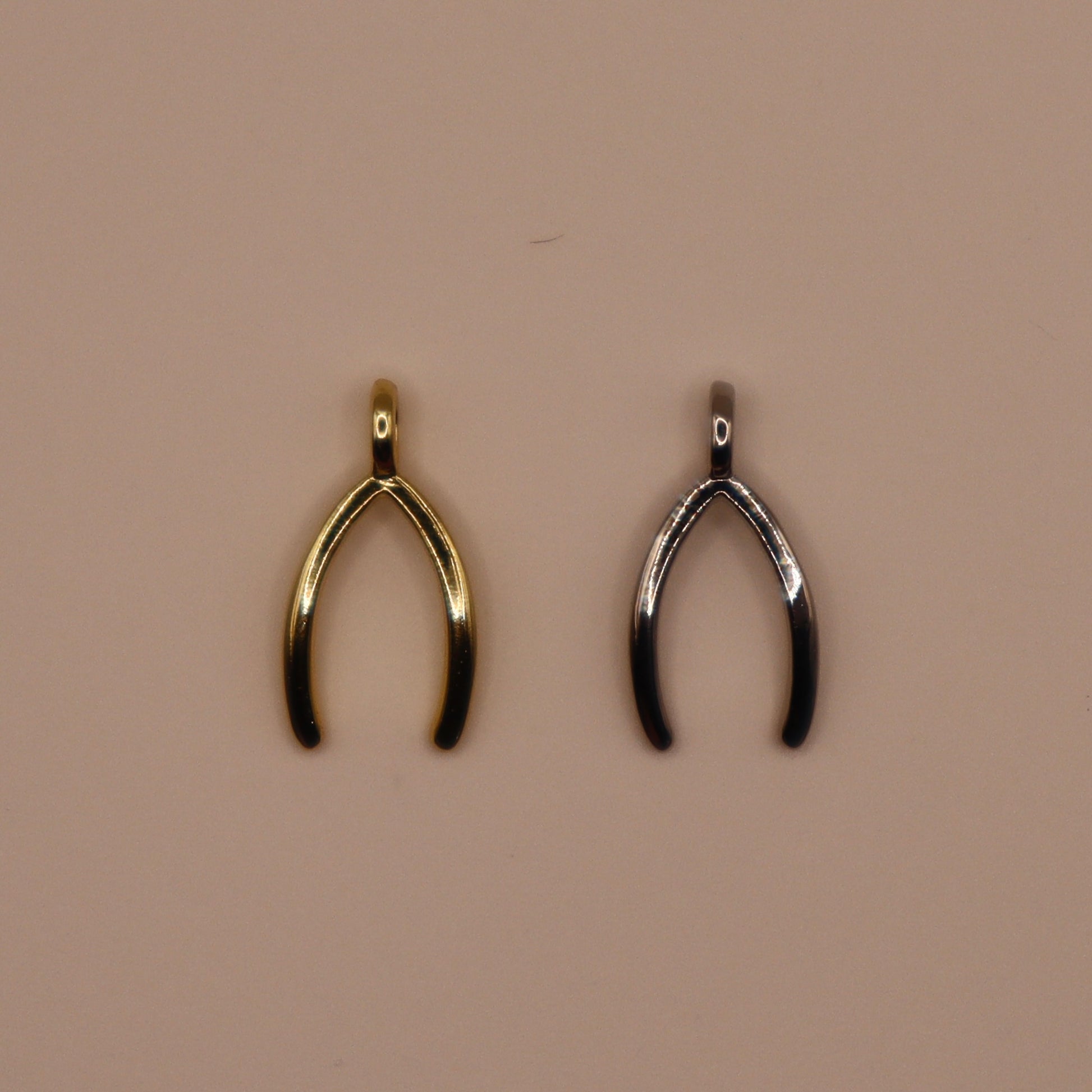 Gold and silver wishbone-shaped pendants on a beige background