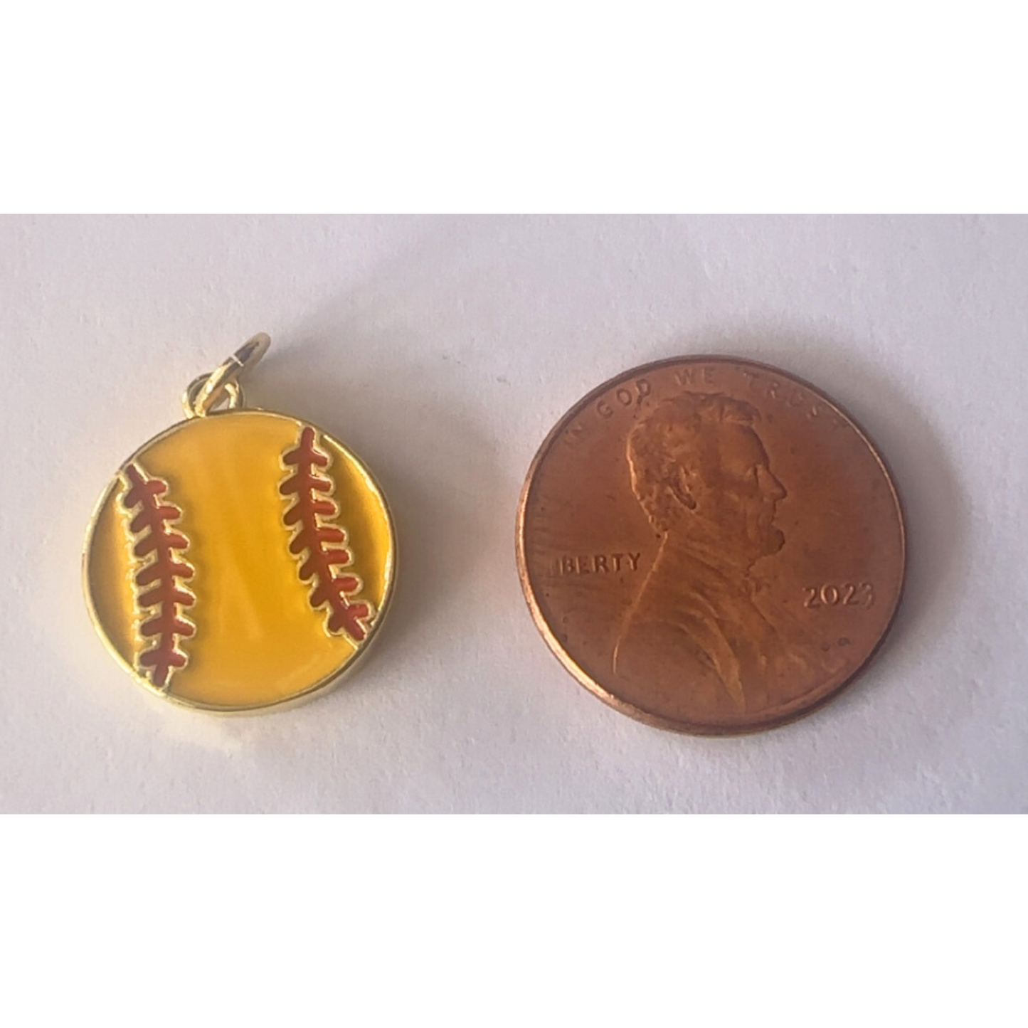 Gold softball pendant next to a penny on a white background