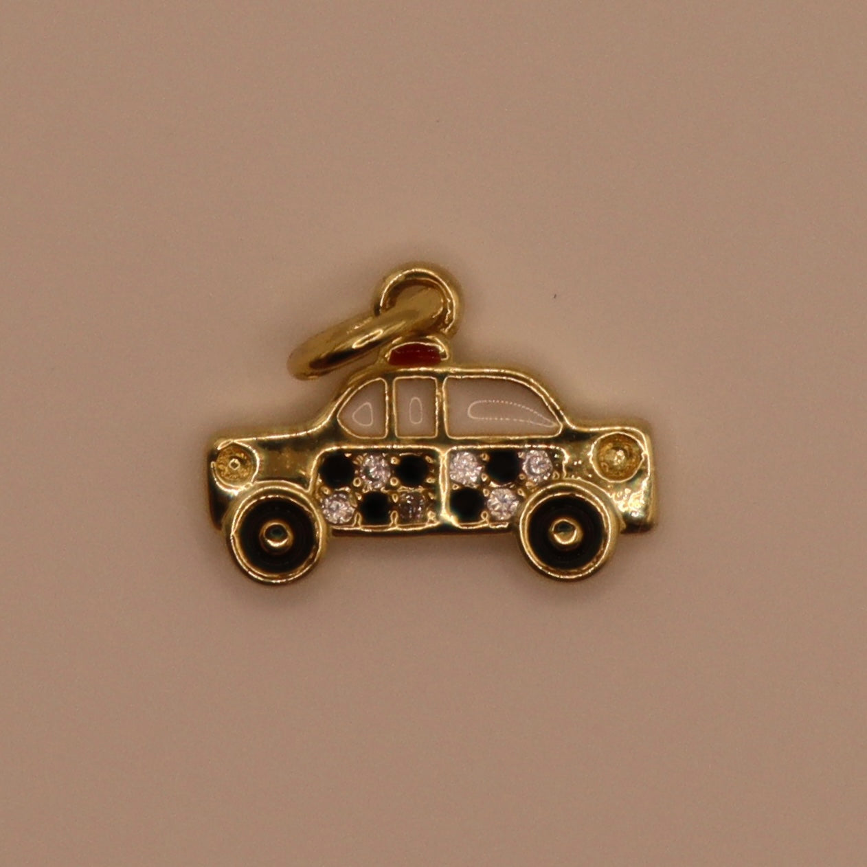 Gold taxi charm with embedded stones on a beige background