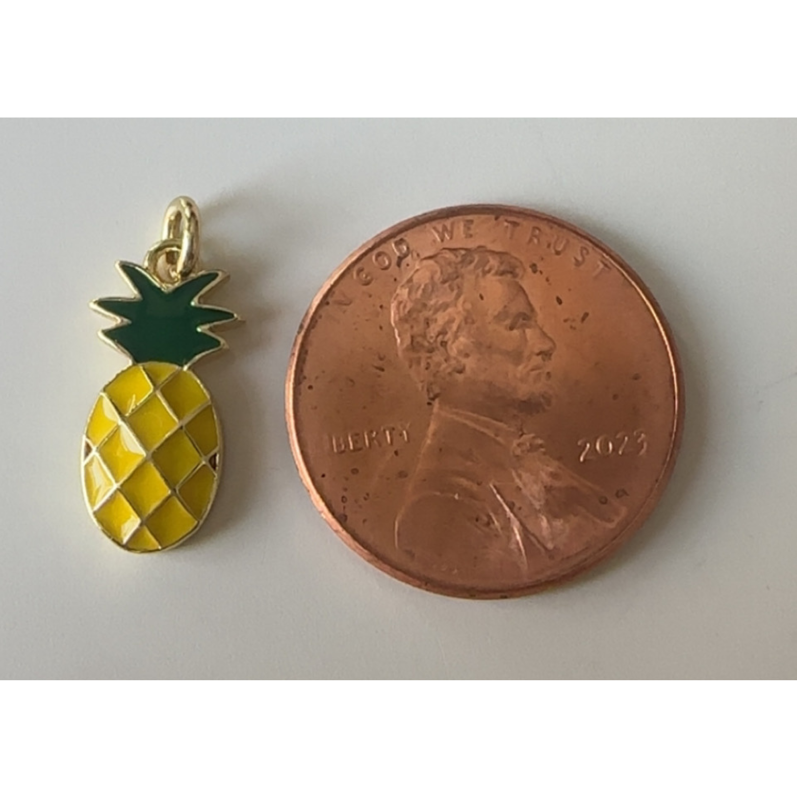 Pineapple-shaped pendant next to a penny on a white background