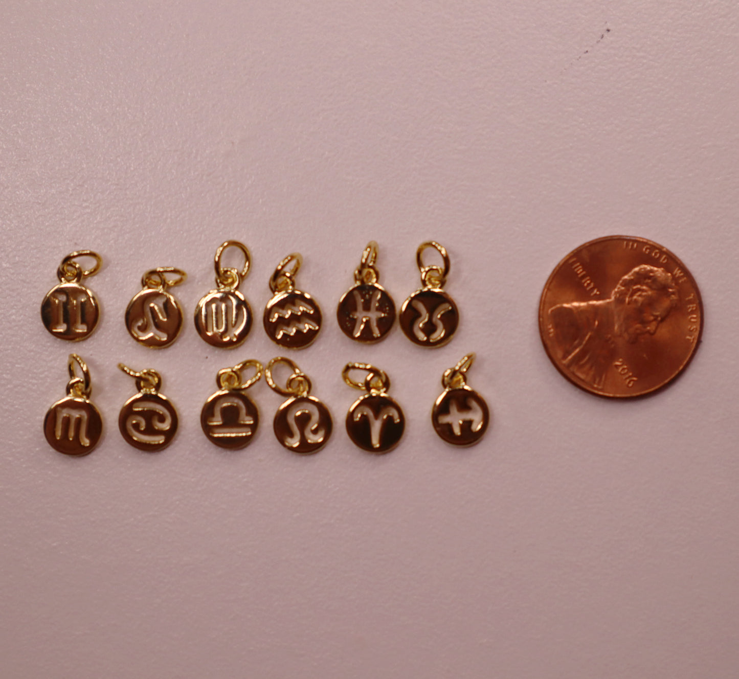 Gold charms with symbols next to a penny on a light pink background