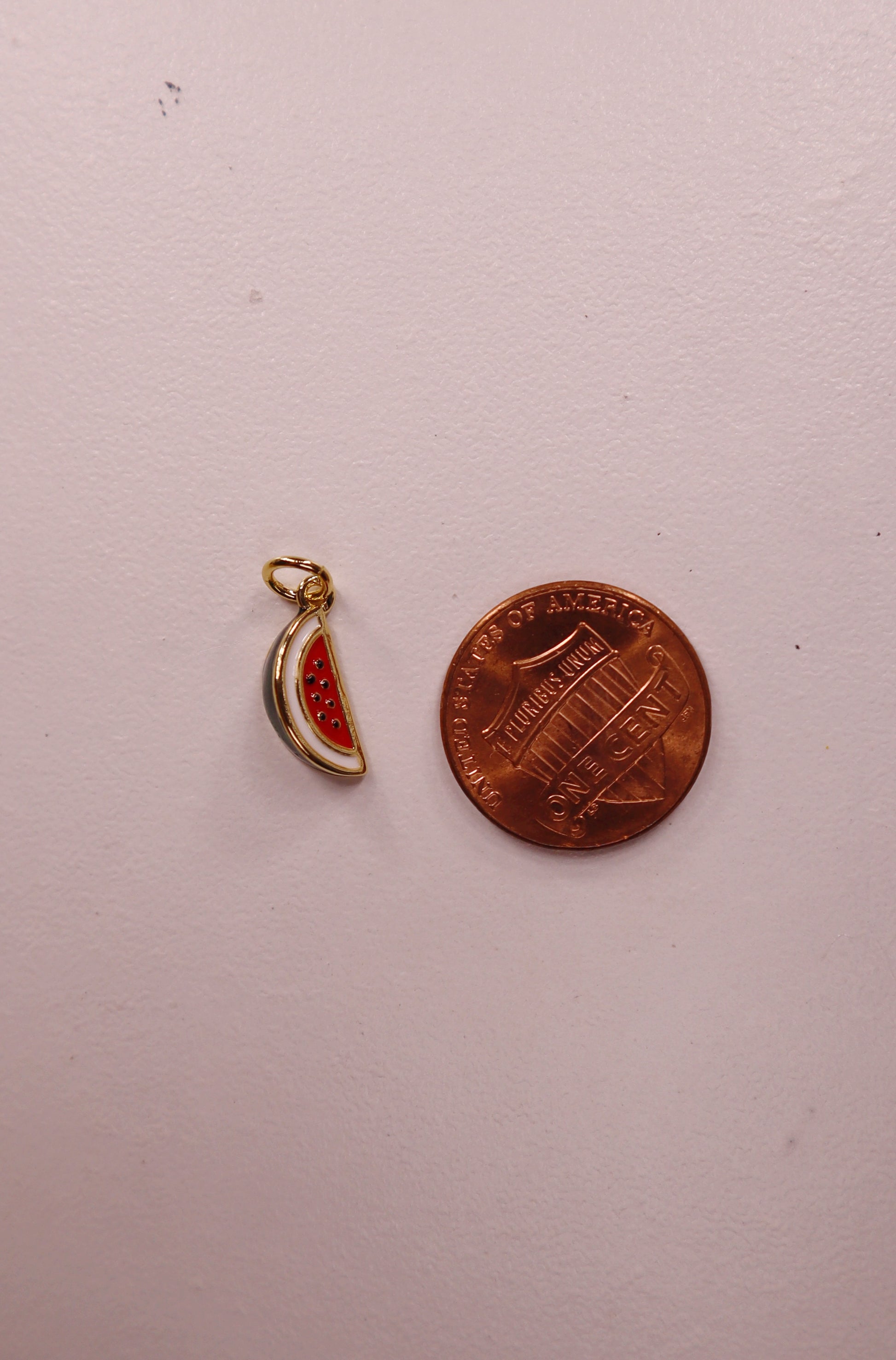 gold and red watermelon pendant next to a penny on a white background