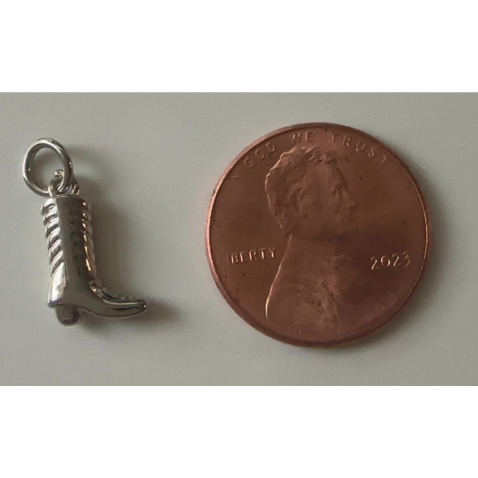 Silver boot charm next to a penny on a light gray background