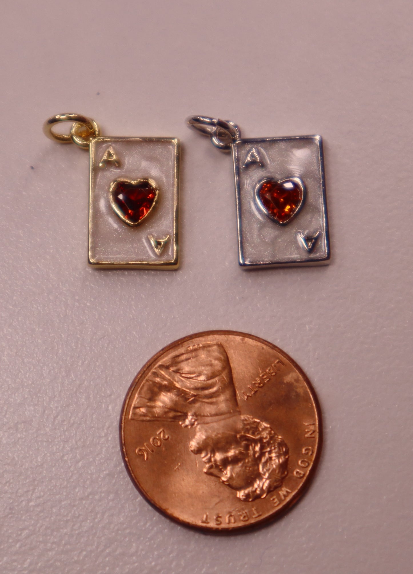 Two playing card suit charms with heart stones next to a penny for scale on a gray background