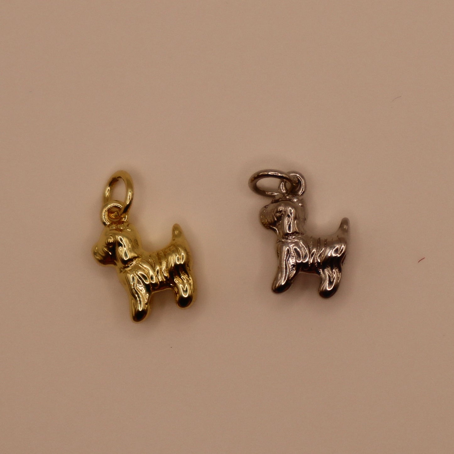 Two dog-shaped charms, one gold and one silver, on a beige background.
