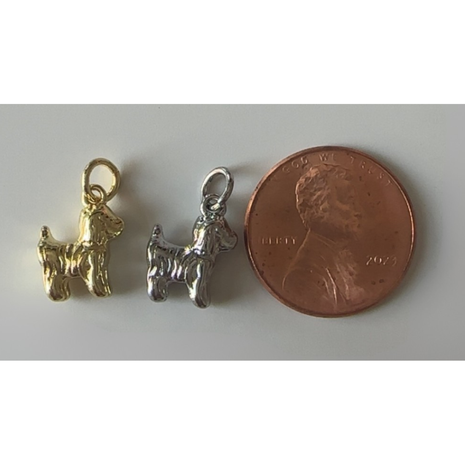 Two dog-shaped charms next to a penny on a gray background