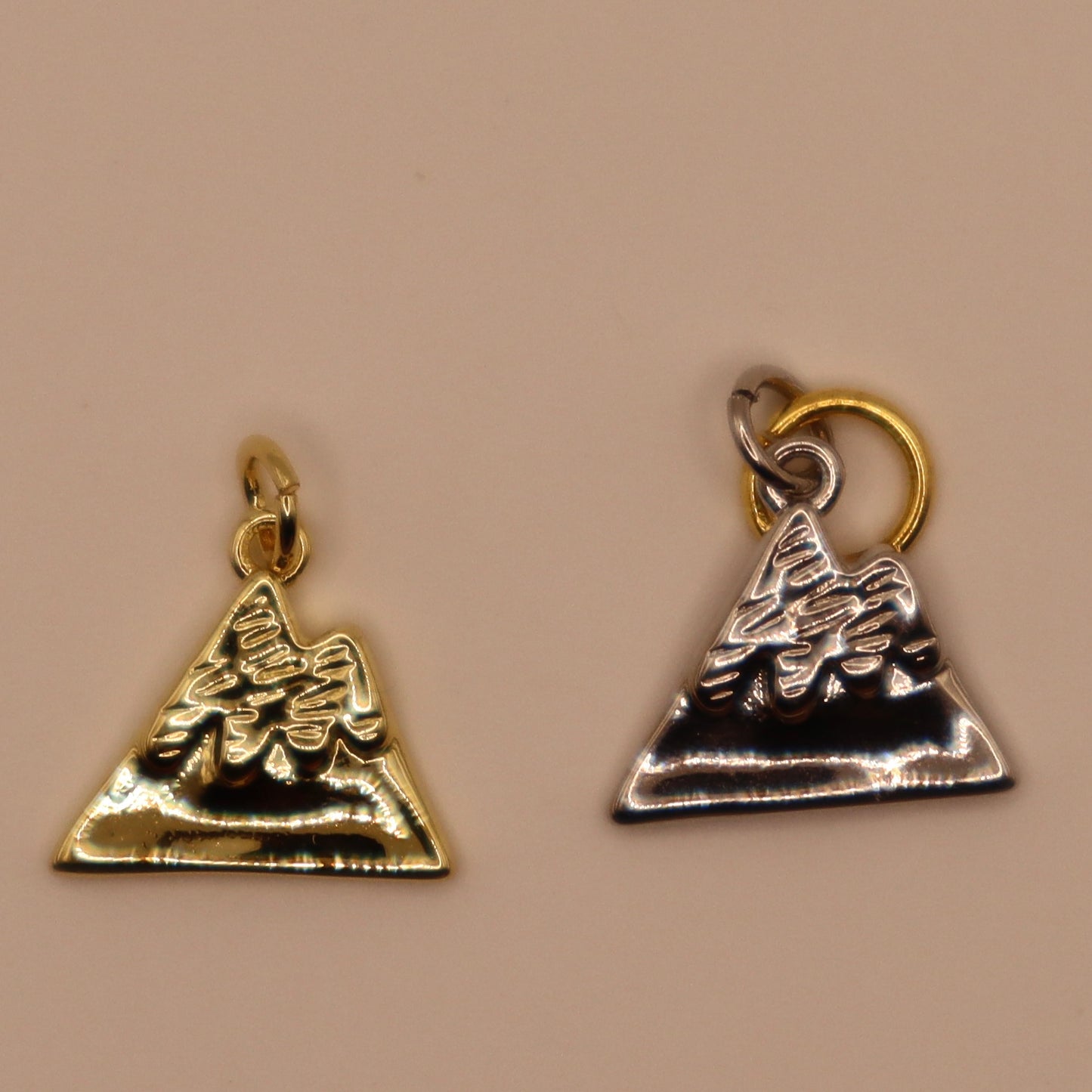 Two mountain charms, one gold and one silver, on a beige background