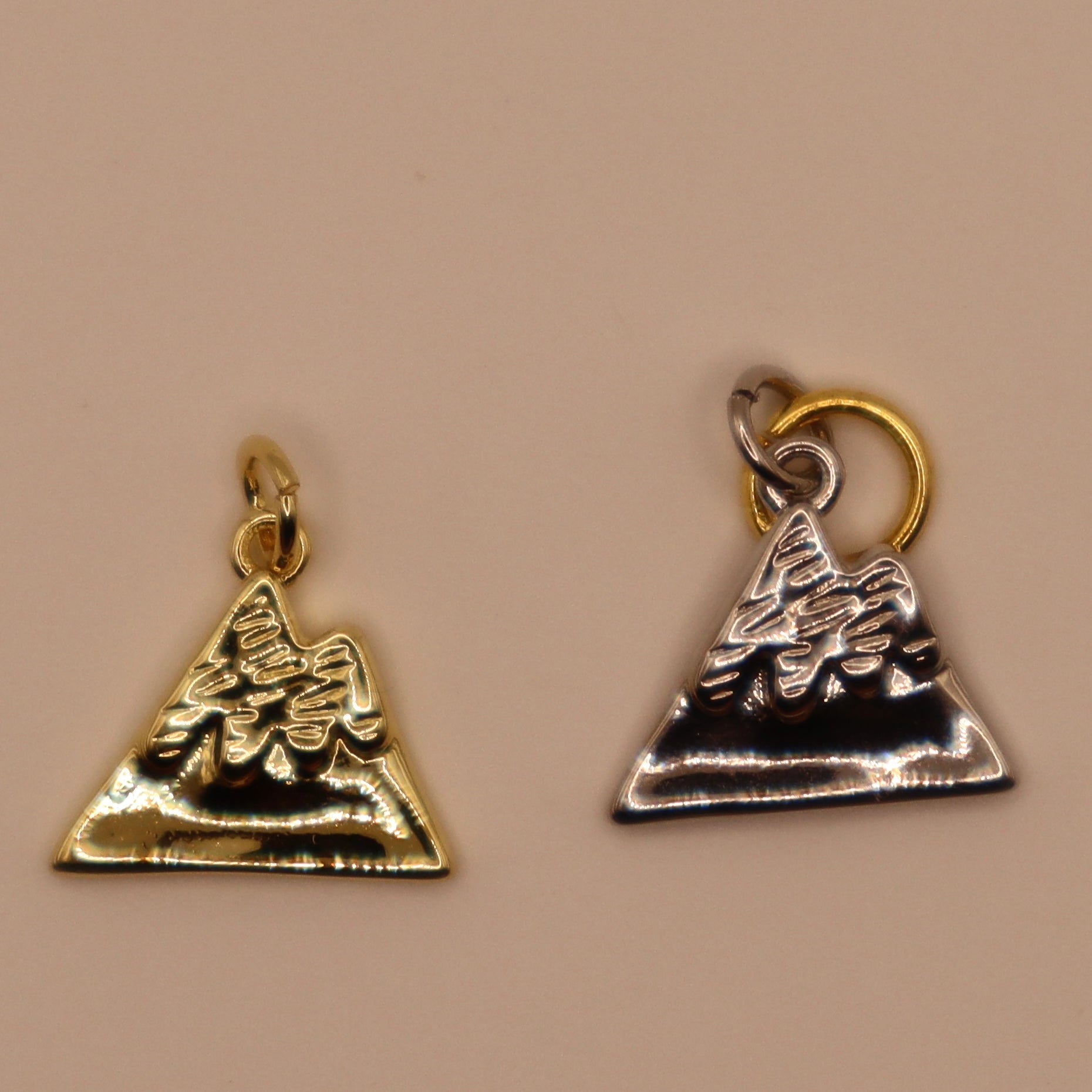 Two mountain charms, one gold and one silver, on a beige background