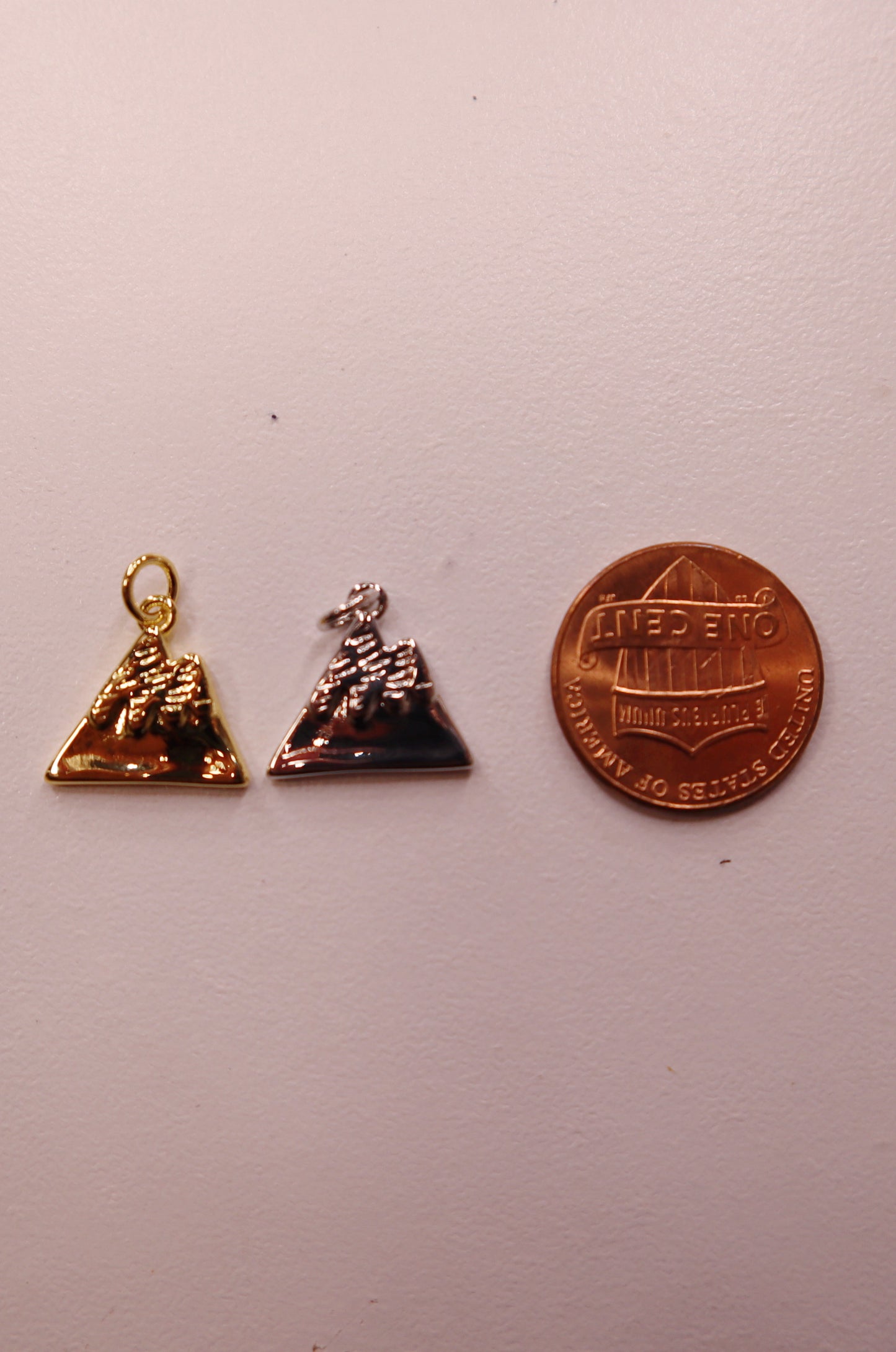Two mountain charms and a penny for scale on a white background