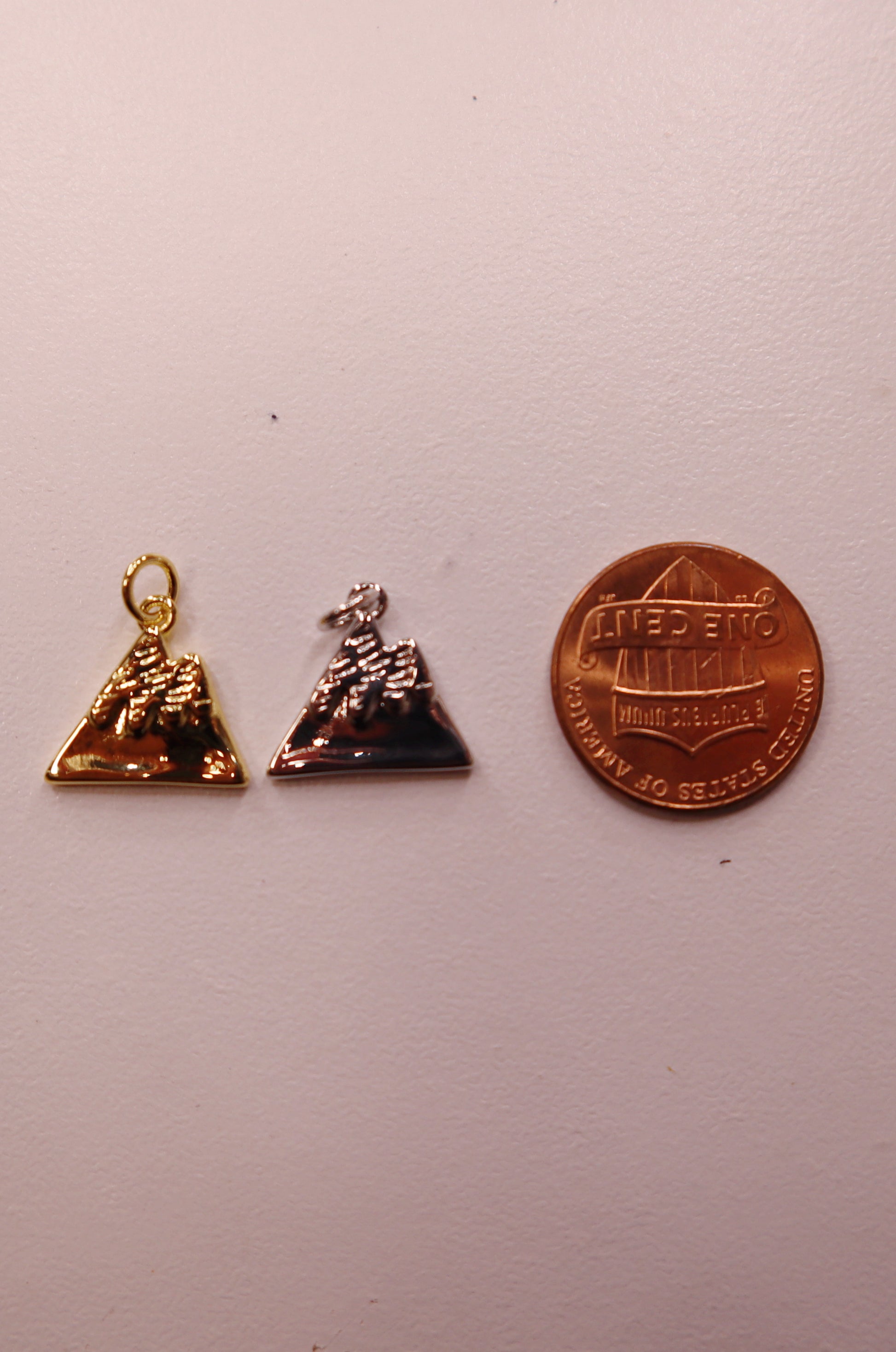 Two mountain charms and a penny for scale on a white background