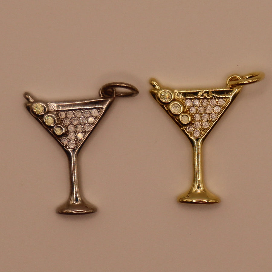 Two martini glass-shaped charms, one gold and one silver, on a beige background.
