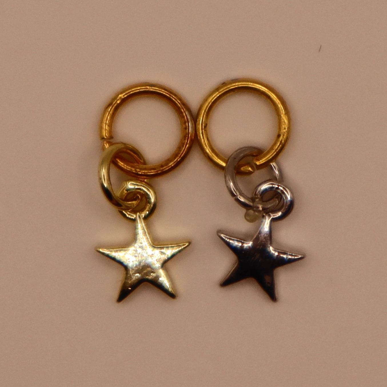 Two star-shaped charms, one gold and one silver, on a beige background.
