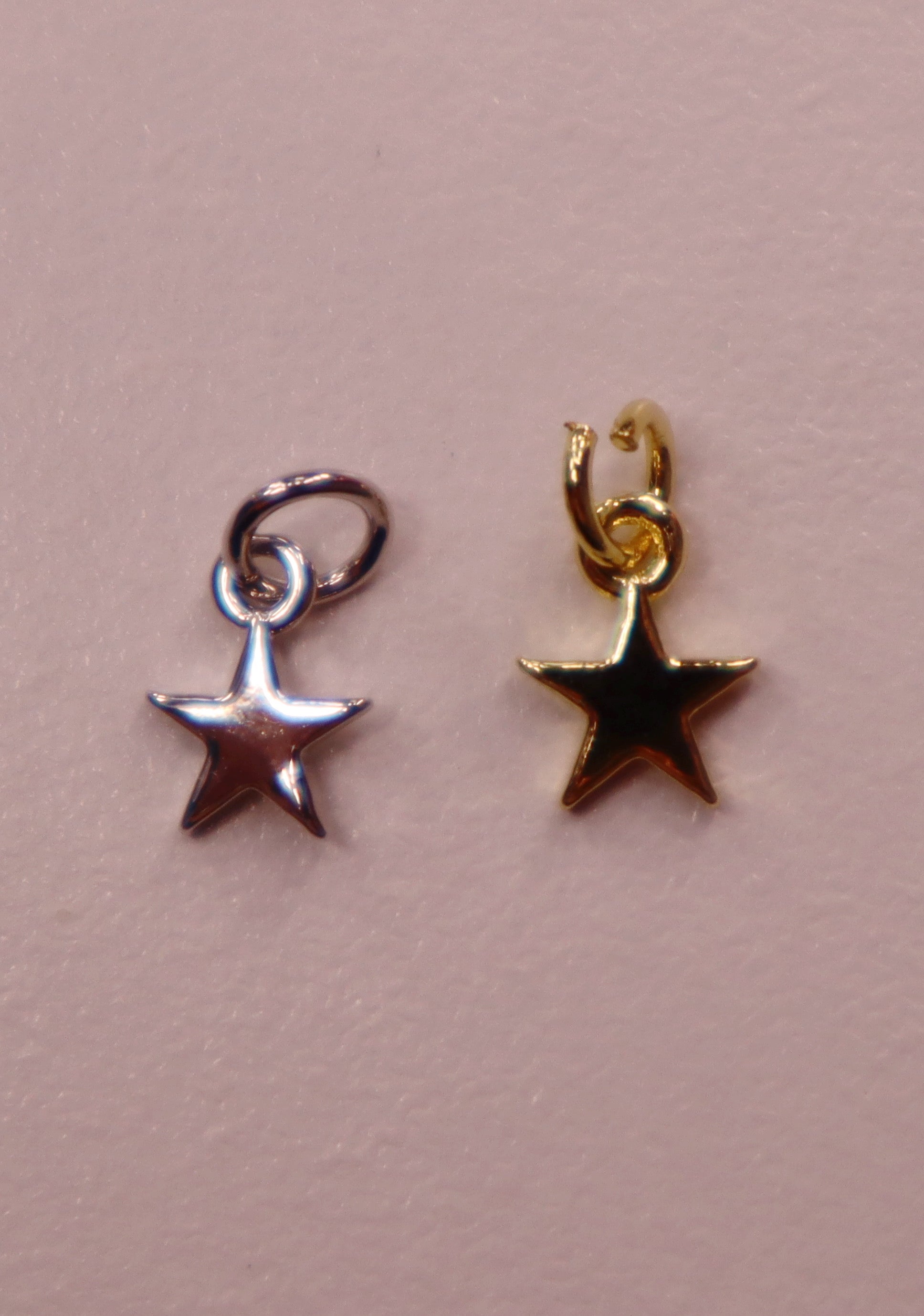 Two star-shaped charms, one silver and one gold, on a pink background.