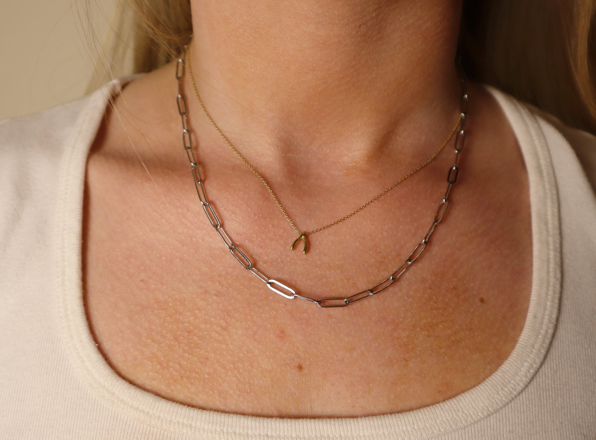 paperclip silver Necklace with a small pendant on a person wearing a beige top.