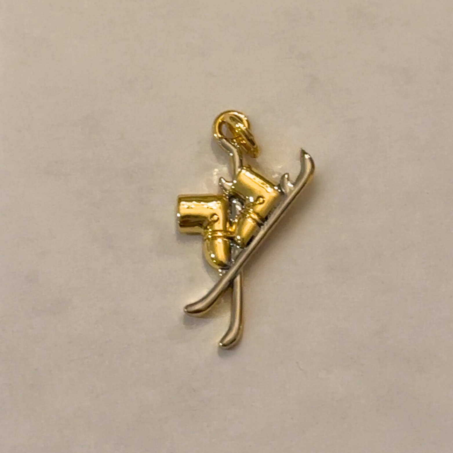 Gold and silver charm of a ski boots on a beige background