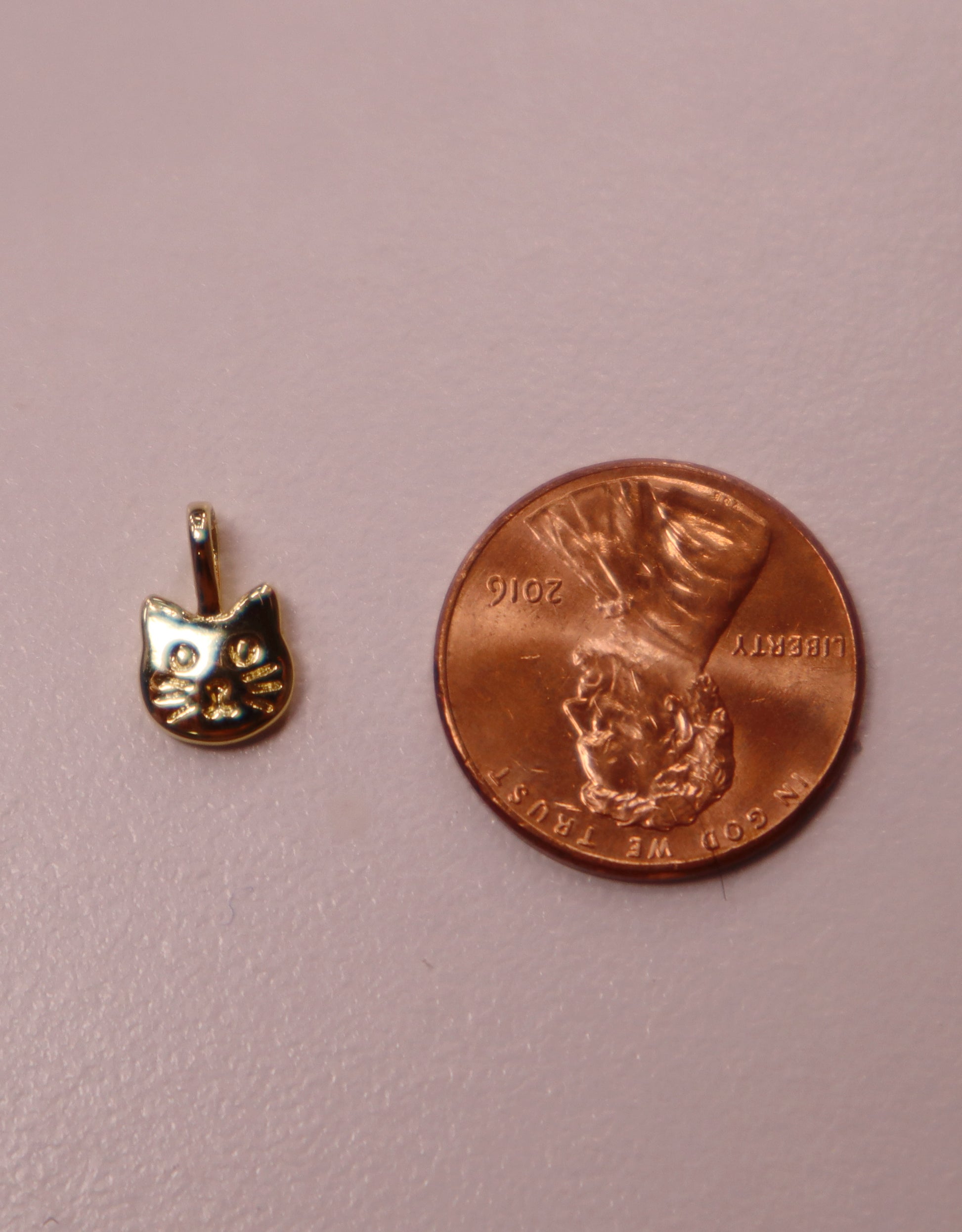 Small gold cat pendant next to a penny on a pink background