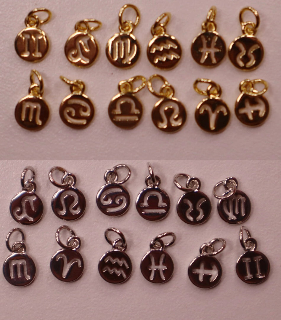 Collection of zodiac charm pendants in gold and silver on a light background